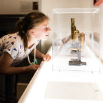 Young child peering at a microscope in a case
