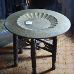 View looking down onto decorative metal tray round table top on carved wooden legs