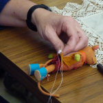 close up of hand holding needle and thread with a small soft toy